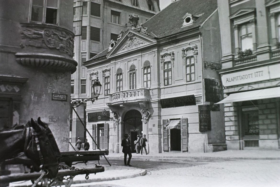 Piarista (Kötő) utca a mára megszűnt Városház térről nézve, szemben a Péterffy-palota / Krist-ház (később itt található a Százéves Étterem), jobbra mellette a Vasudvar. 1912. Fortepan / Schmidt Albin